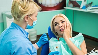 A young female holding her cheek in pain while talking to the dentist